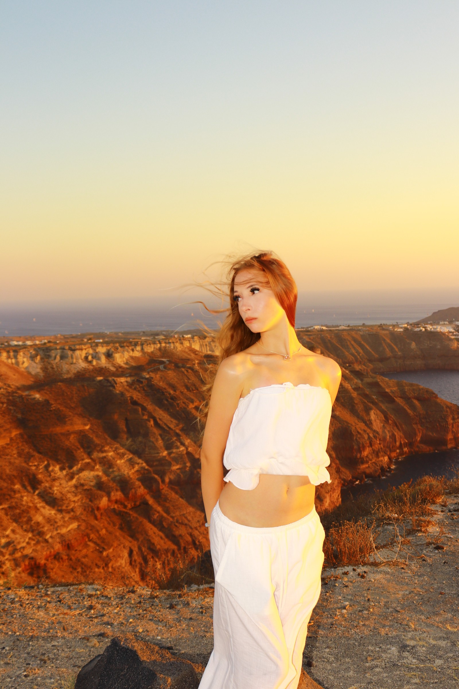 Natalie in a white outfit at a sunlit coastal viewpoint